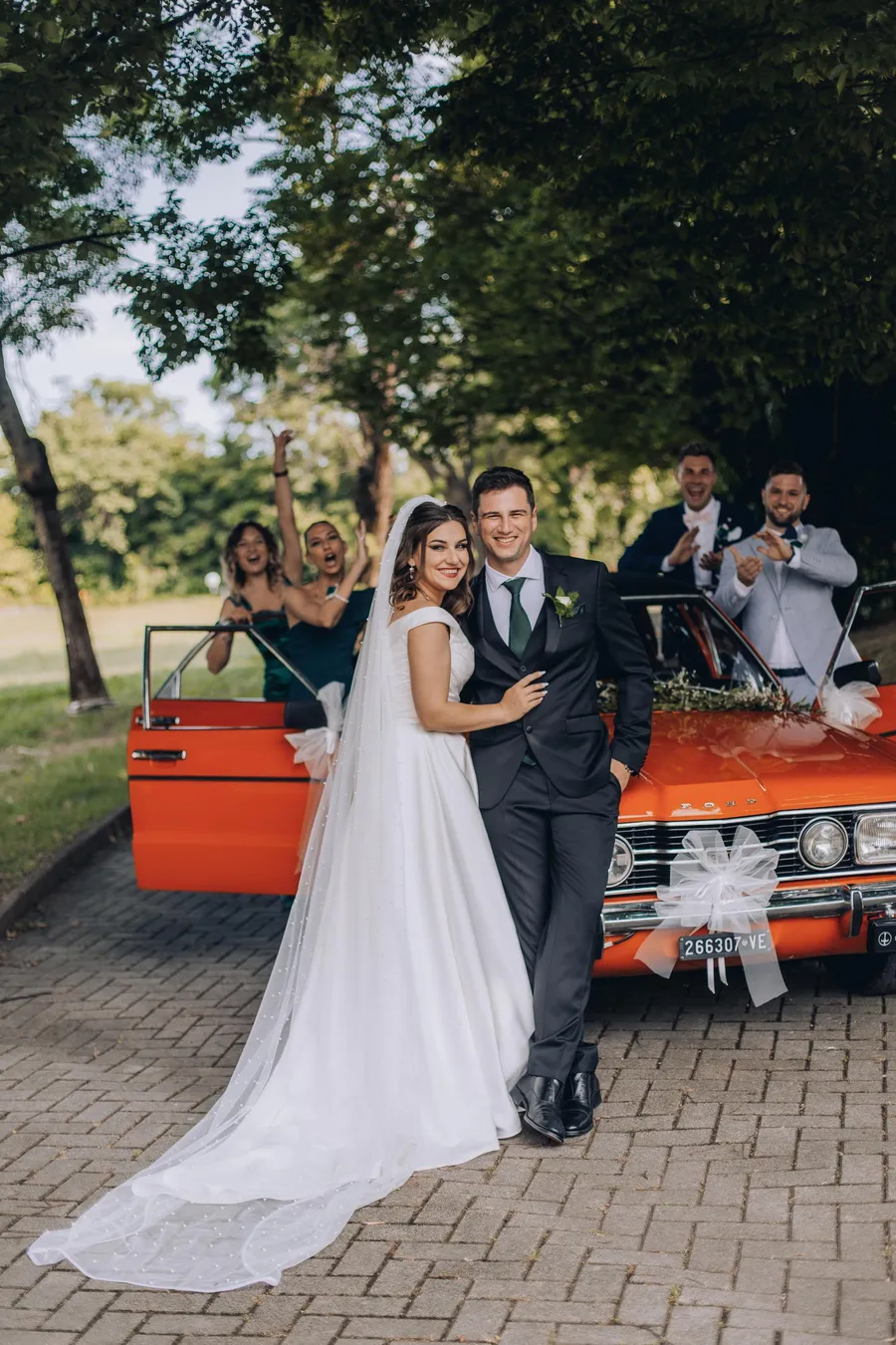 Wedding couple posing beside a red vintage car