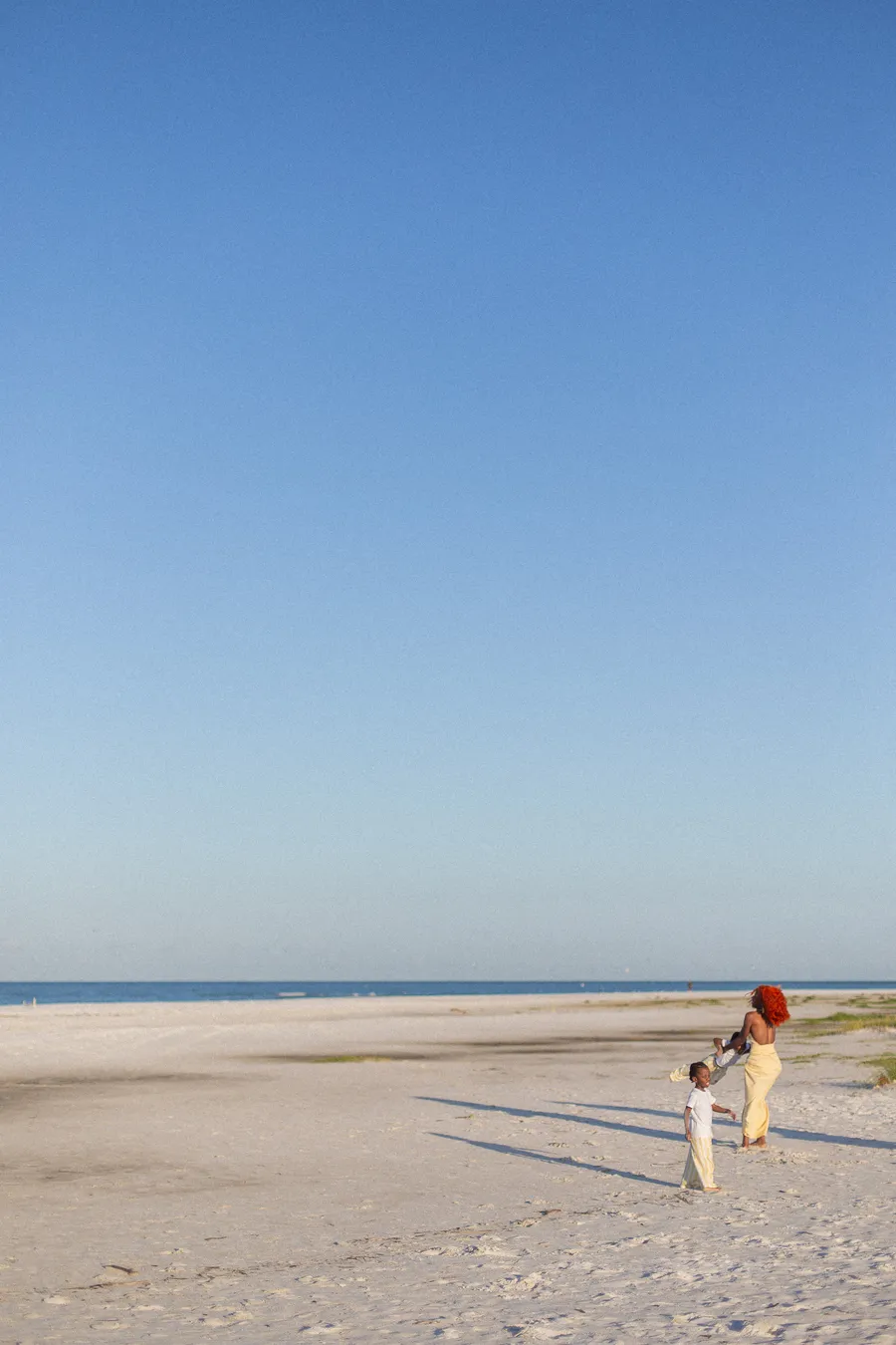 Child running across a quiet beach beneath a clear blue sky