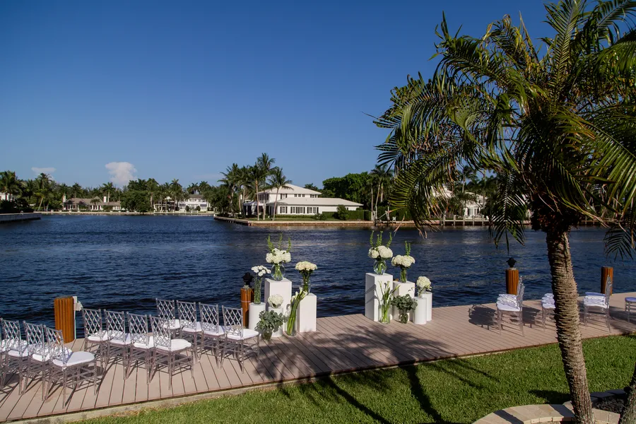Waterfront wedding ceremony setup with white flowers and palm trees