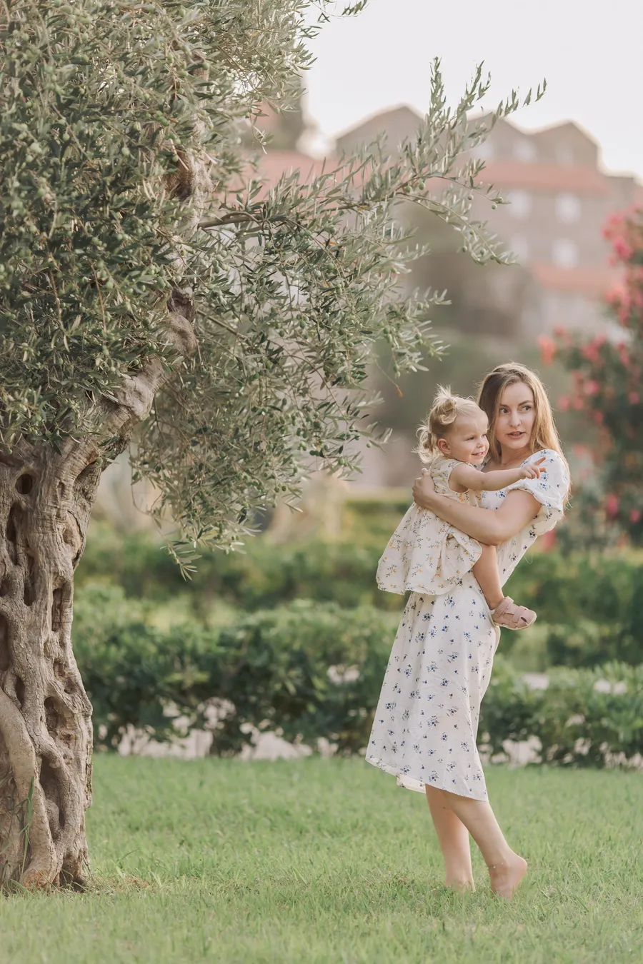 Mother lifting her daughter beside a shaded garden tree