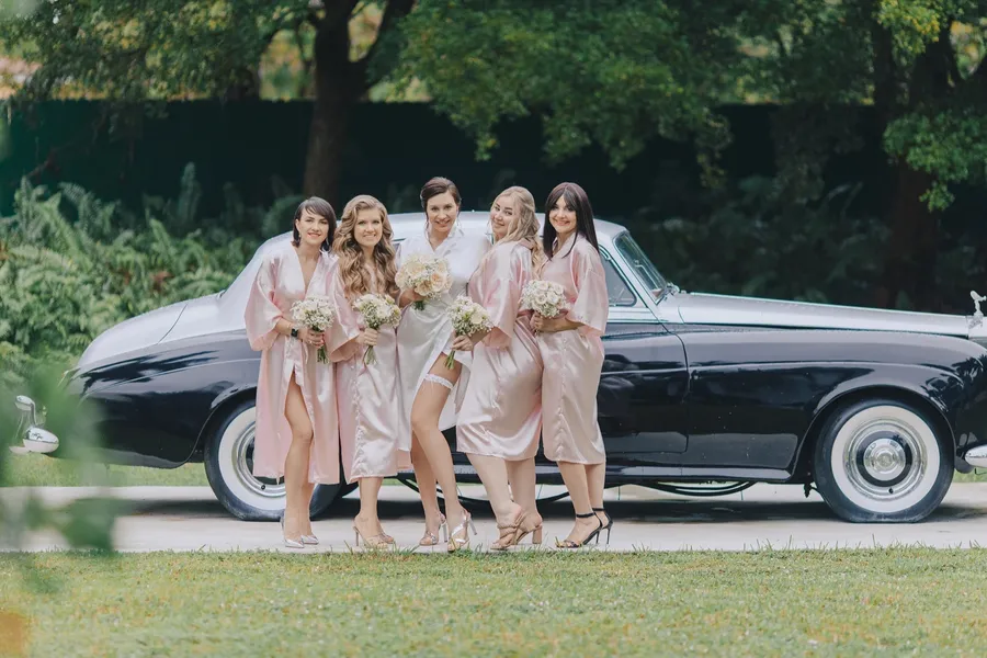 Bridesmaids beside a vintage car during an outdoor wedding
