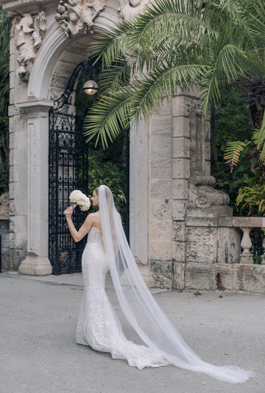 Bride framed by an ornate garden gate and palm trees