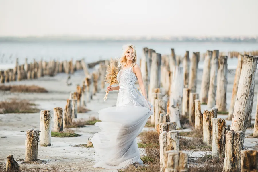 Natali Terentieva standing in a wedding dress near weathered coastal pilings
