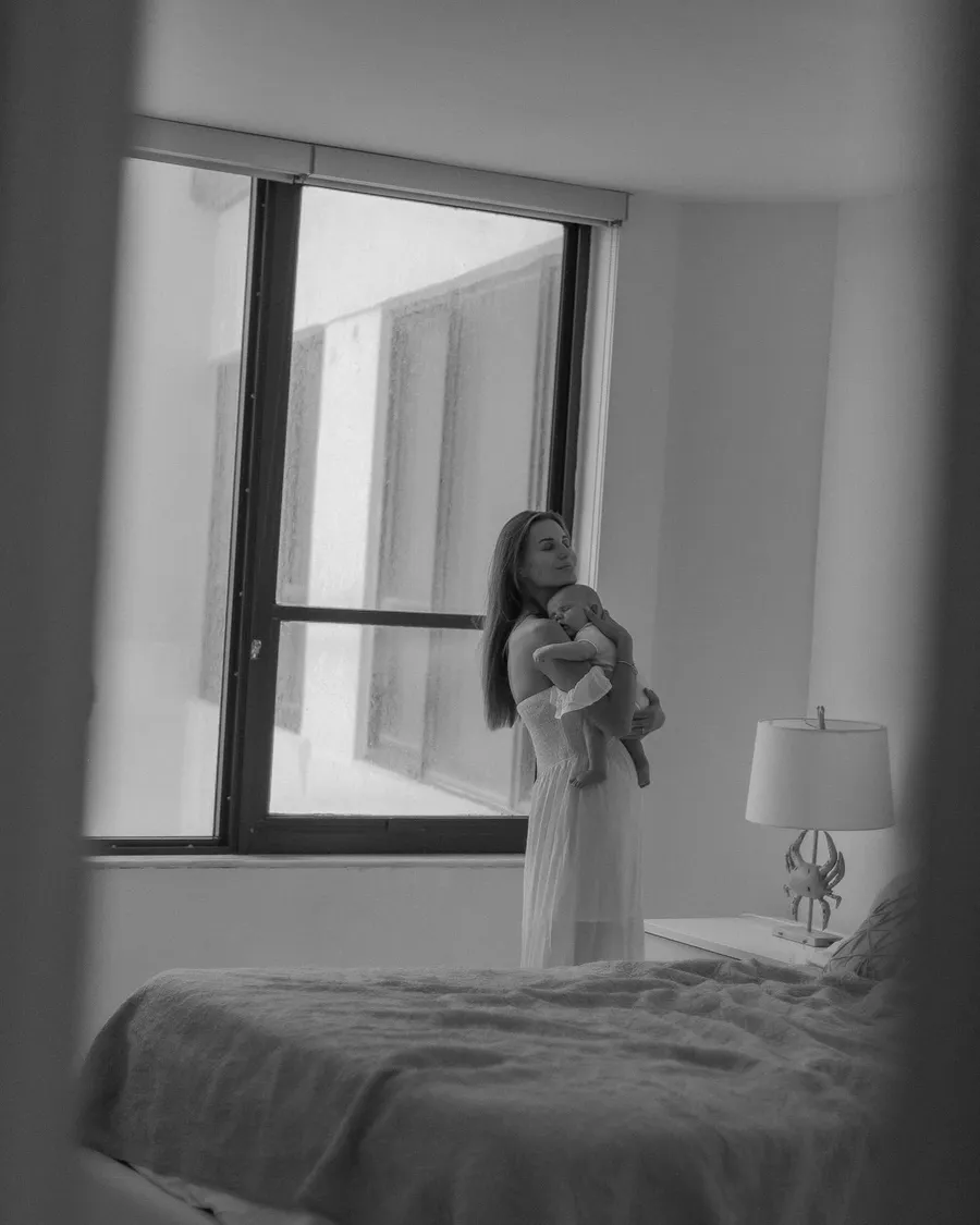 Black-and-white lifestyle portrait of a mother and baby by a window