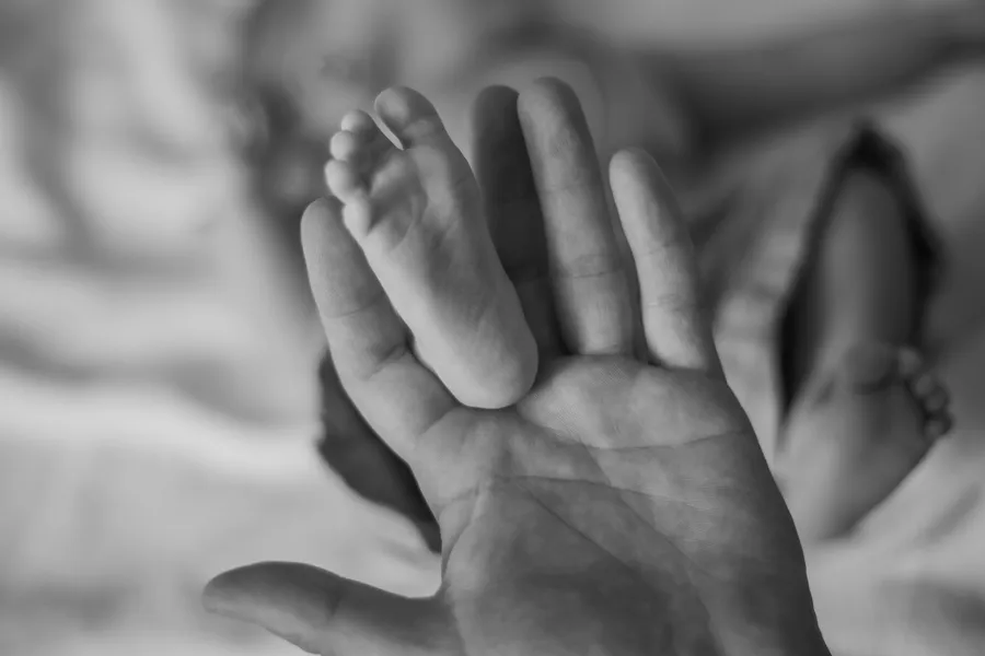 Black-and-white detail of a newborn baby’s hand in a parent’s palm