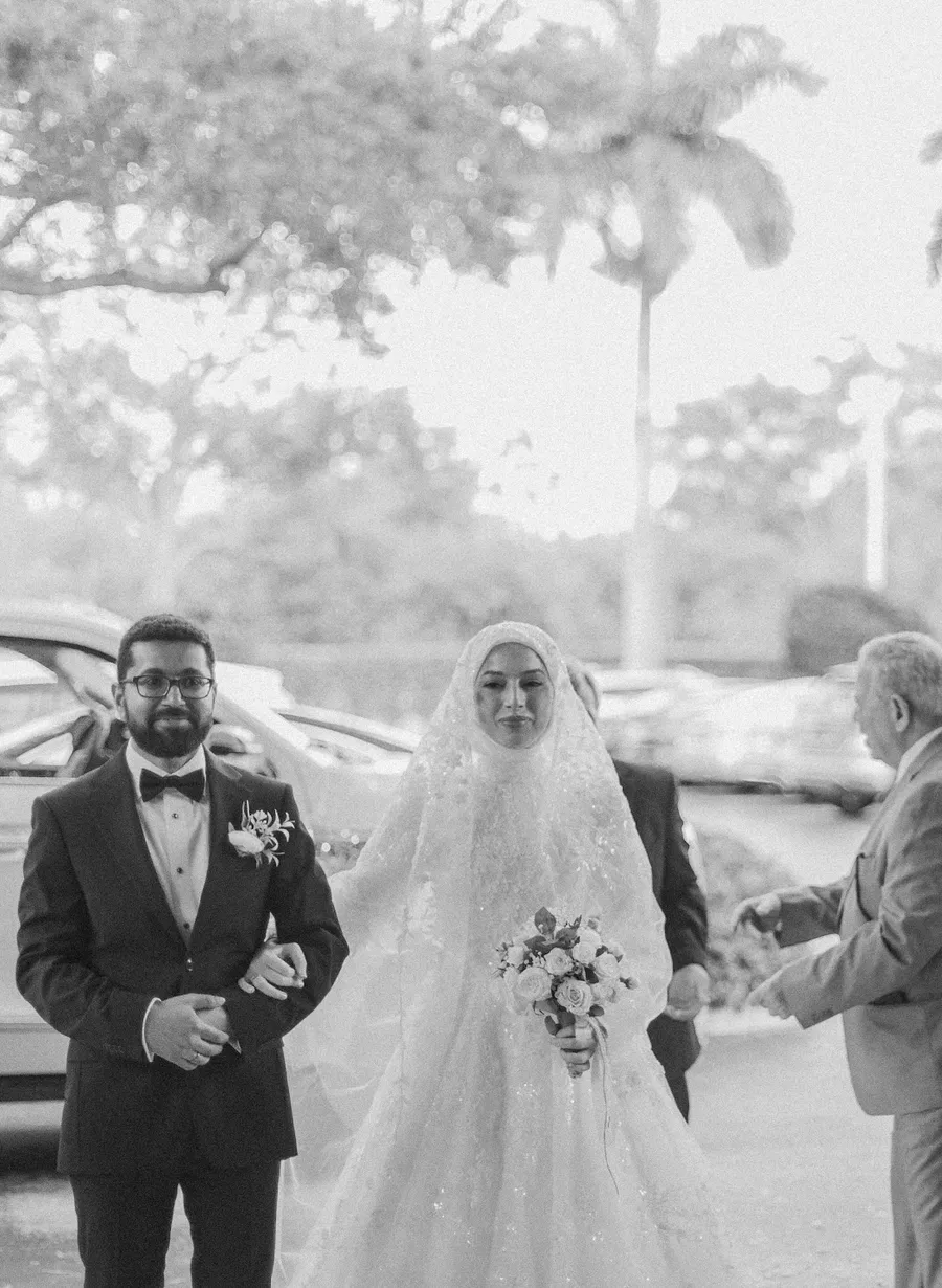 Black-and-white photograph of a bride escorted to the ceremony
