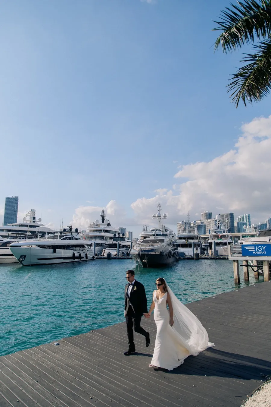 Newlyweds standing on a marina pier with the city skyline beyond
