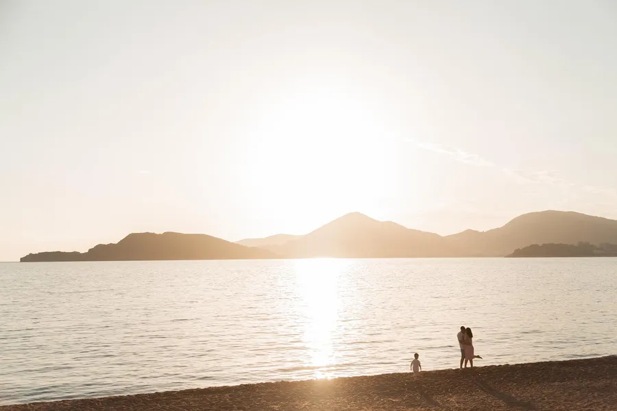 Family silhouetted against the sun over calm coastal water