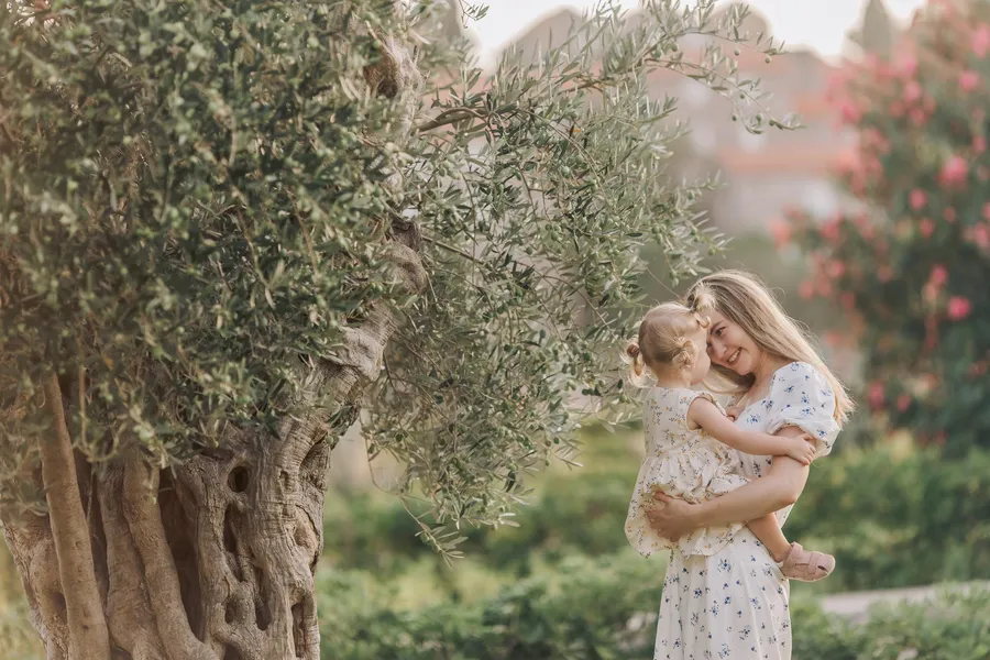 Mother holding her daughter beneath an olive tree