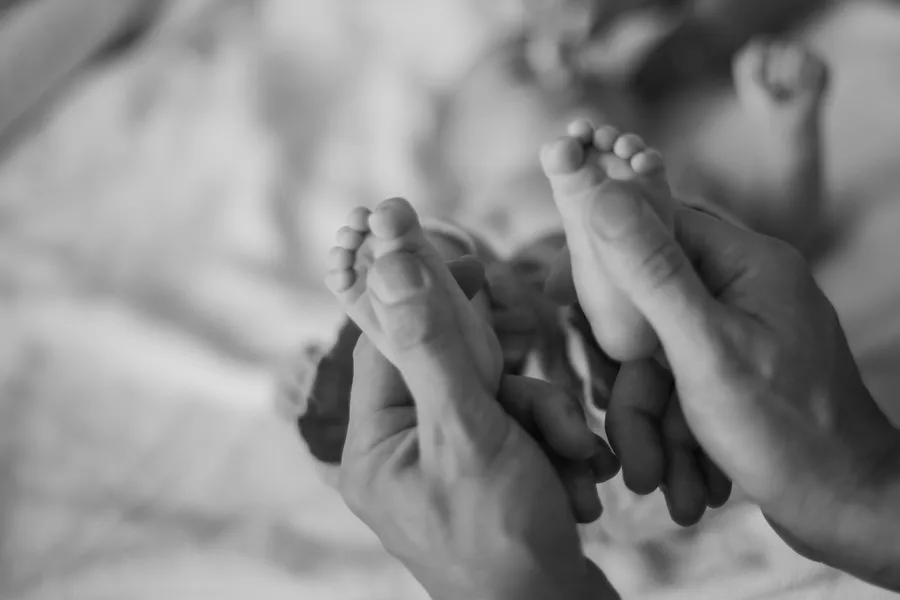 Black-and-white close-up of a newborn holding a parent’s finger